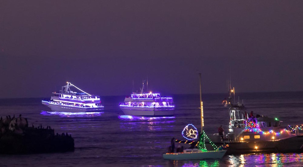Two boats decorated with purple lights on a dark sea, another boat with colorful lights in the foreground.